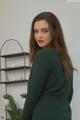 A woman wearing a dark green dress standing in front of a shelf.