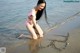 A woman in a pink bathing suit writing in the sand on the beach.