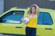 A woman holding a soccer ball in front of a yellow car.