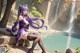 A woman with long purple hair sitting on a ledge next to a waterfall.