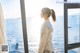 A woman standing in front of a window looking out at the ocean.