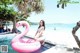 A woman in a bikini sitting on an inflatable flamingo.