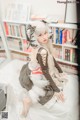 A woman sitting on a bed in front of a book shelf.