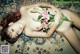 A naked woman laying on a rug holding a flower.